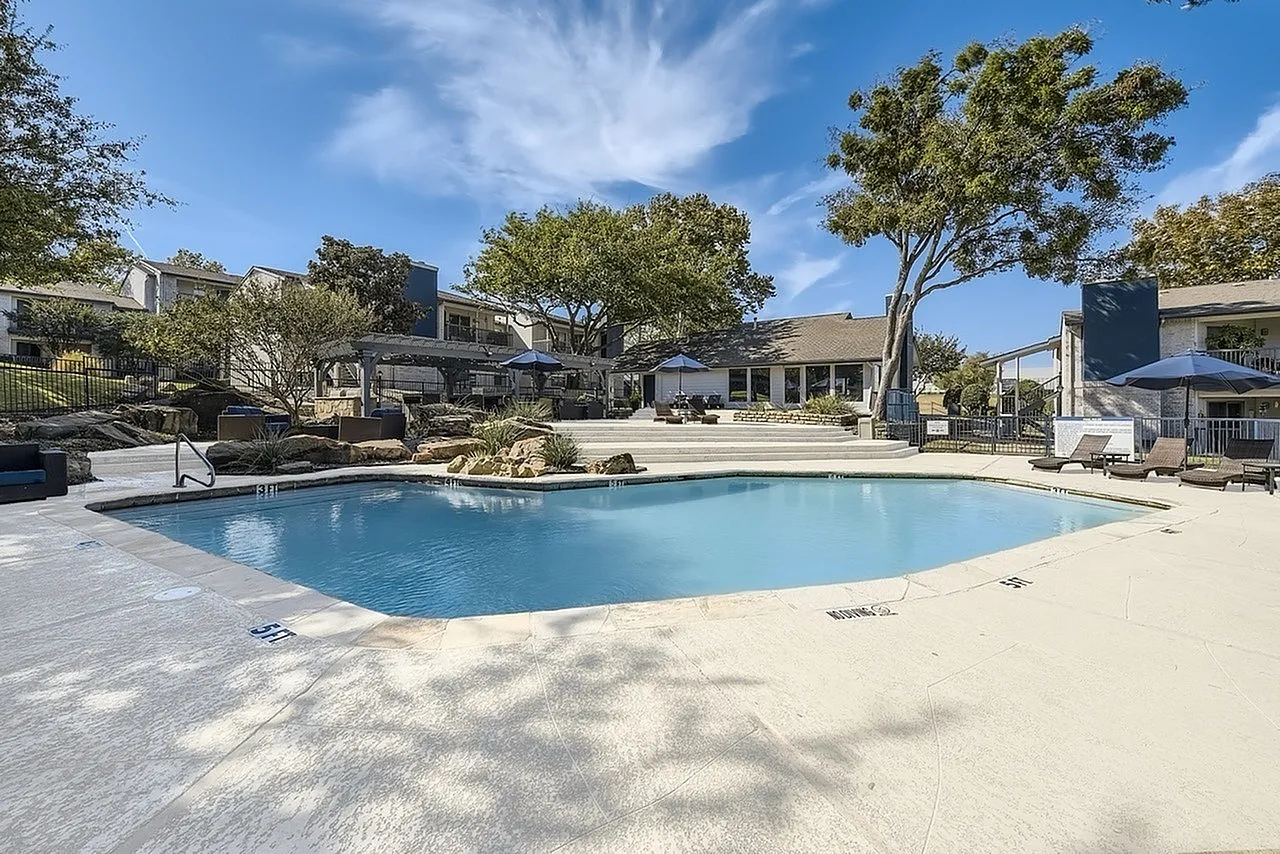 Pool deck, landscaped rock feature, patio umbrellas, mature trees