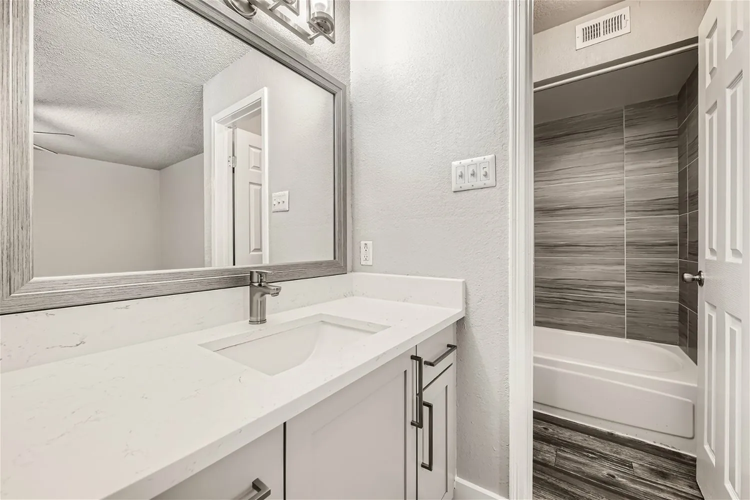 Bathroom vanity, framed mirror, undermount sink, quartz-style countertop, wood-look tile tub surround