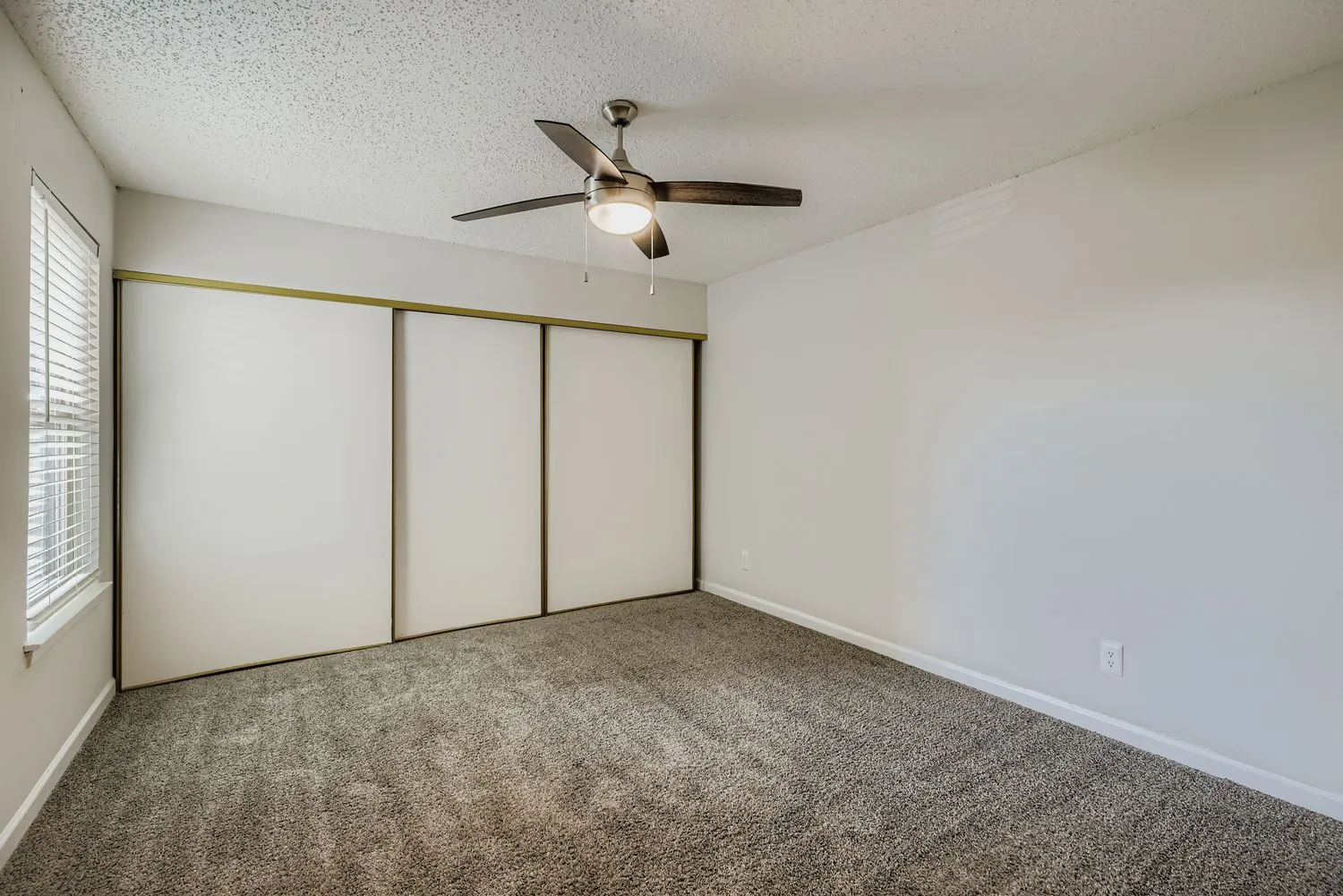 Primary bedroom with carpet flooring, ceiling fan, and sliding closet doors