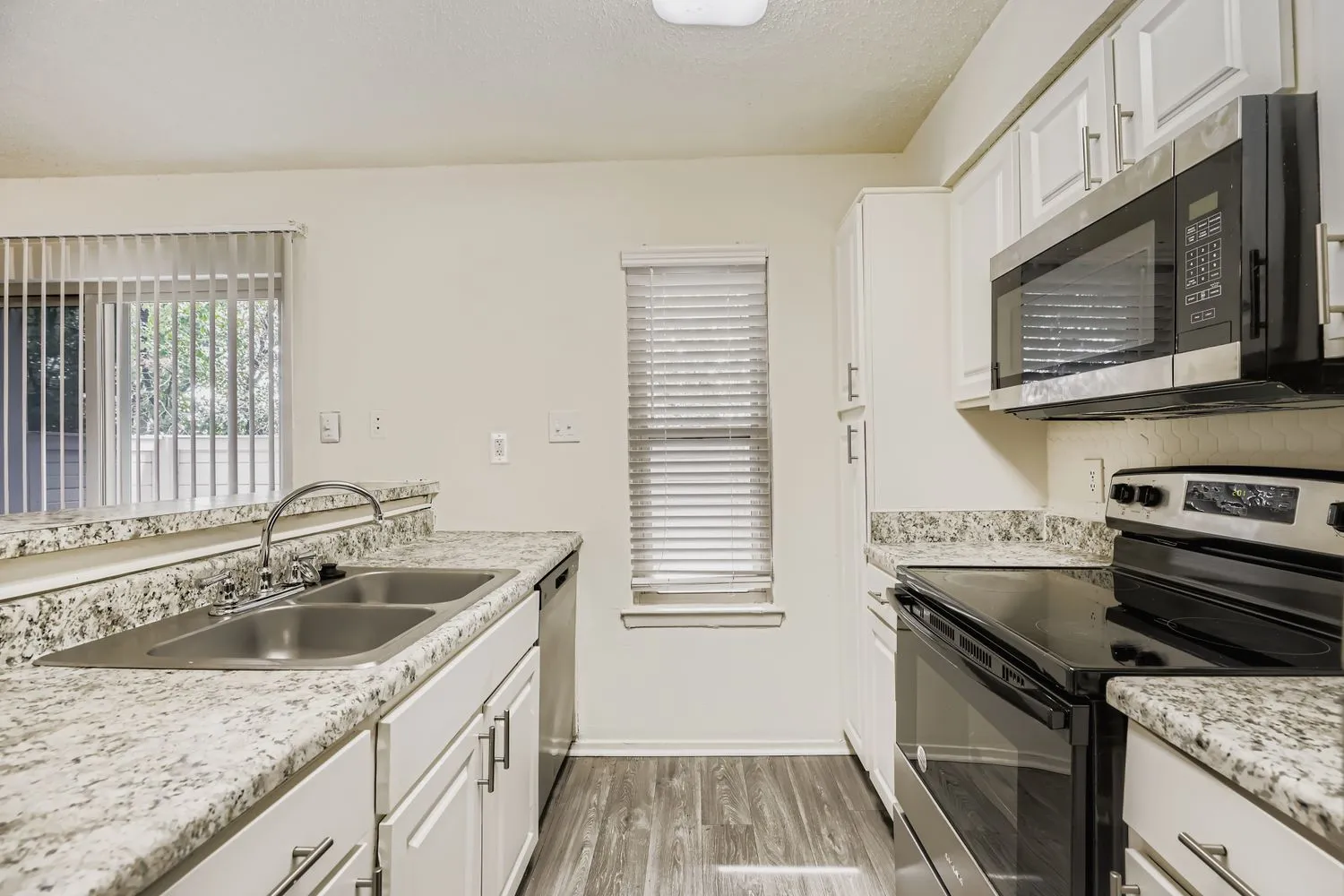 Kitchen with white cabinetry, black appliances, and granite-style countertops