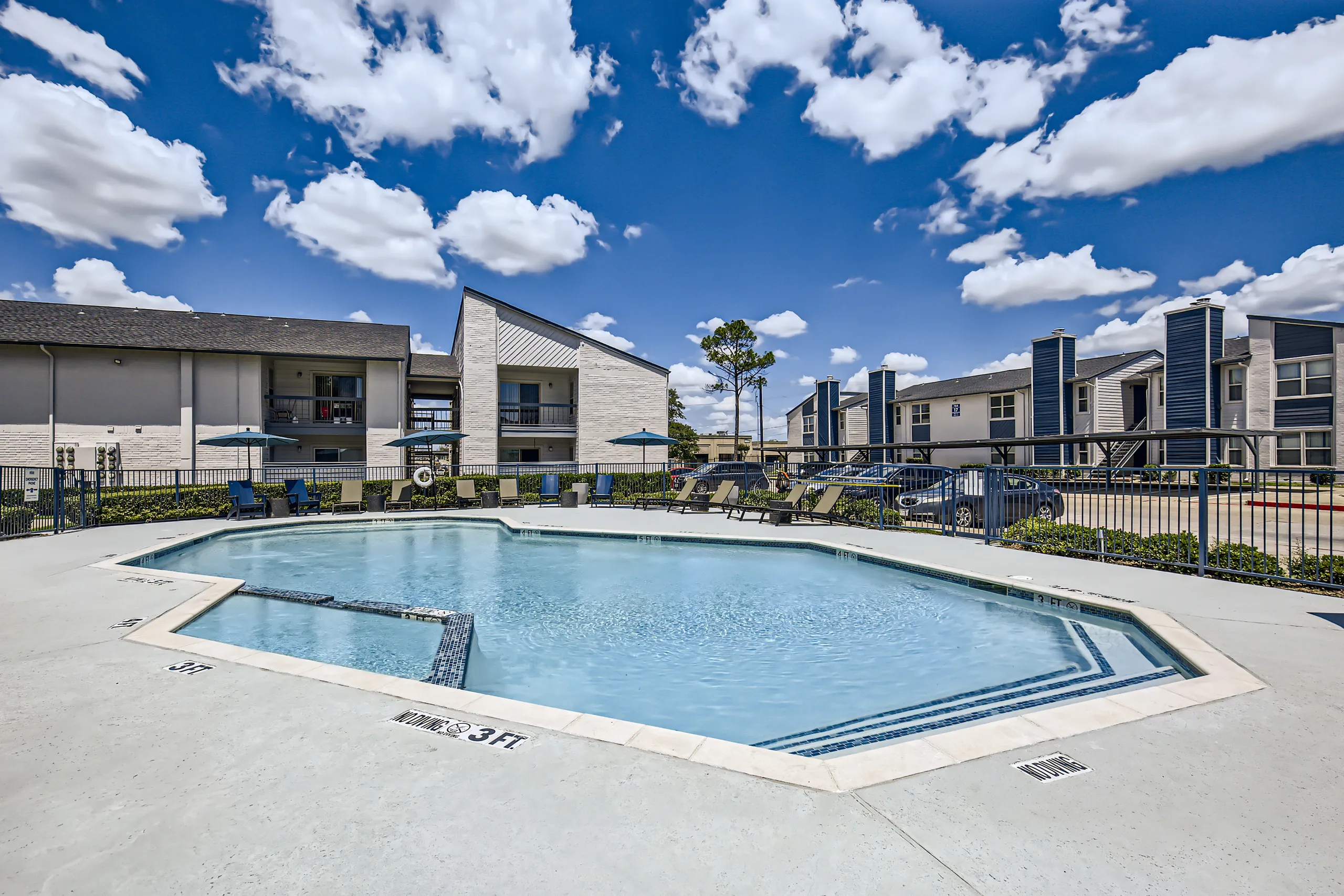 Community pool deck with poolside seating and apartment buildings in background