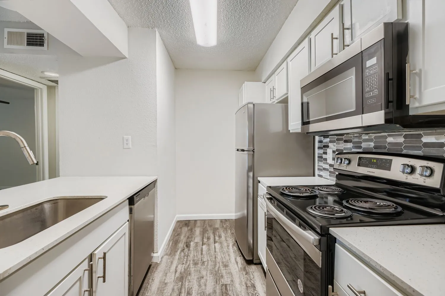 Galley kitchen with white cabinetry, stainless steel appliances, and tile backsplash