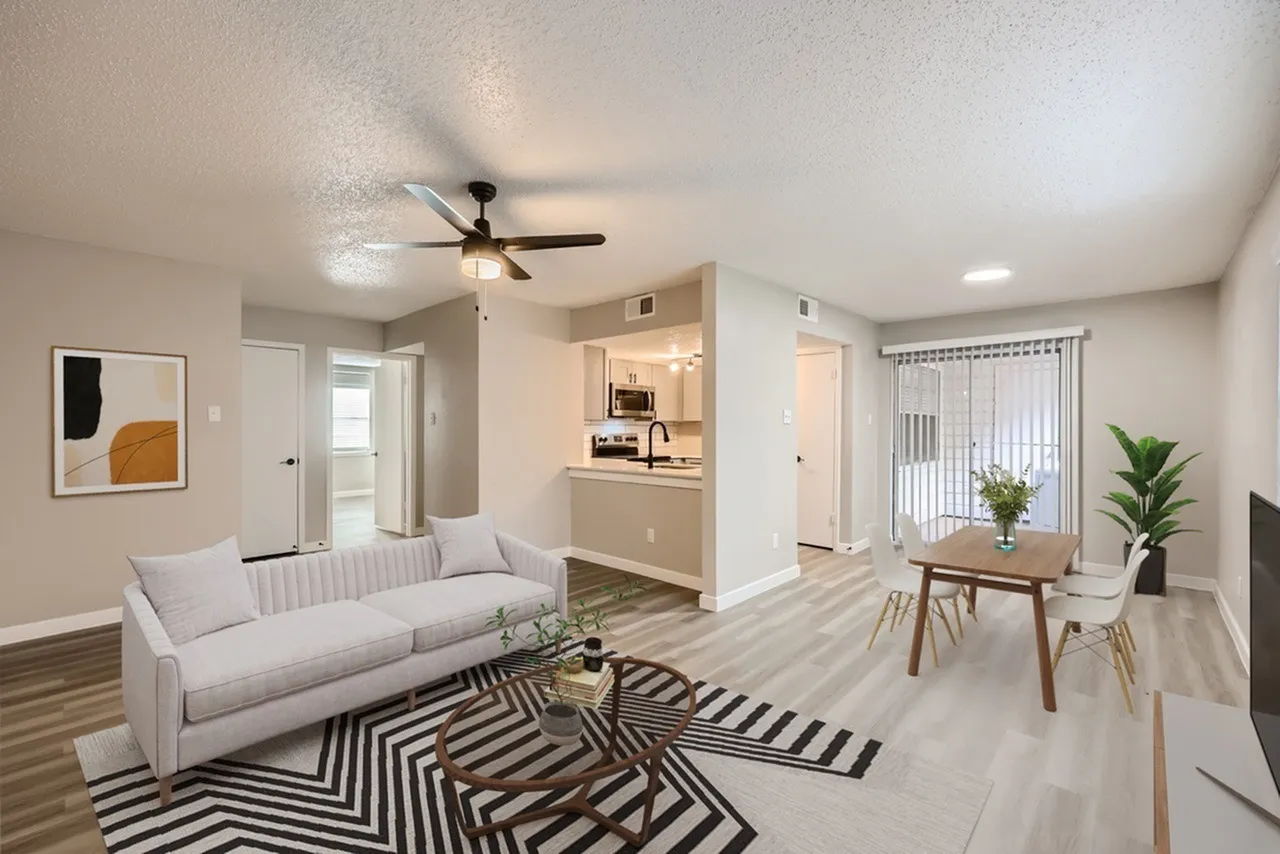 Living room with wood-style plank flooring, light gray sofa, striped area rug, ceiling fan, kitchen with light cabinetry and island