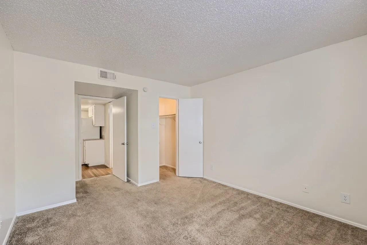 Primary bedroom, carpet flooring, ceiling vent, entry doors to closet and ensuite