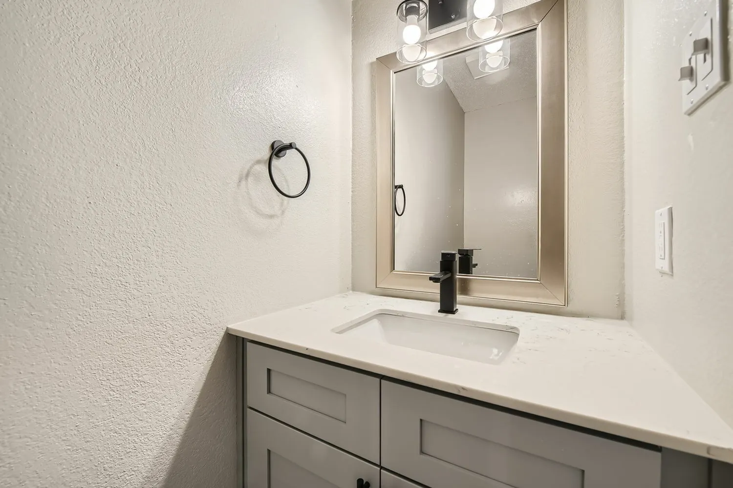 Bathroom vanity, gray cabinetry, white quartz countertop, rectangular sink, framed mirror, vanity lighting