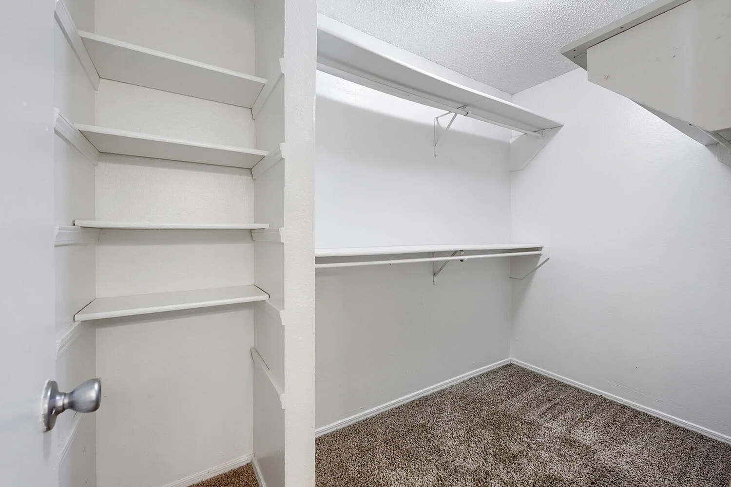 Walk-in closet, white walls, metal shelving, carpet flooring