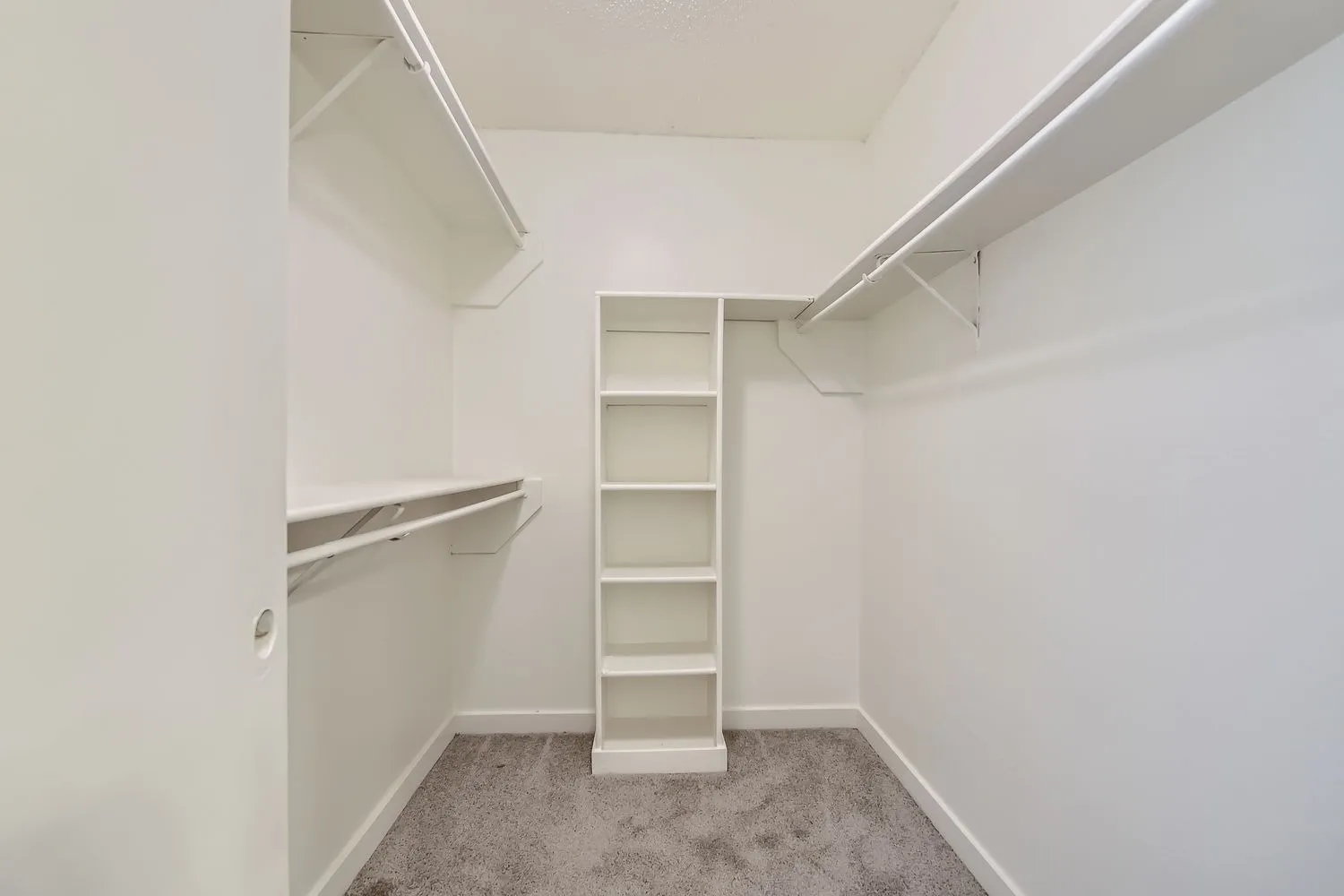 Walk-in closet, white shelving, clothing rods, gray carpet flooring, recessed lighting