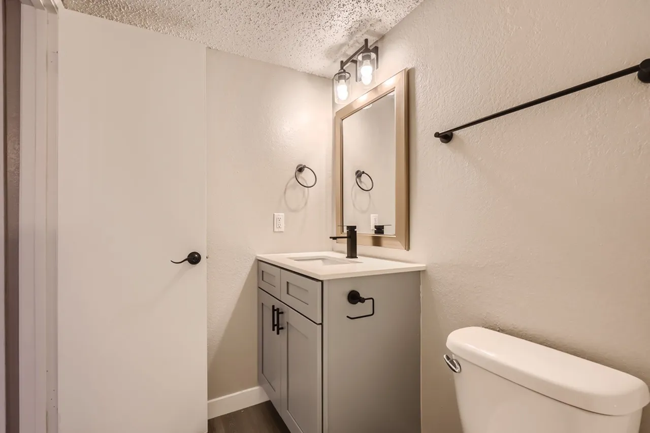 Bathroom, light wood cabinetry, white quartz countertop, framed mirror with vanity lighting
