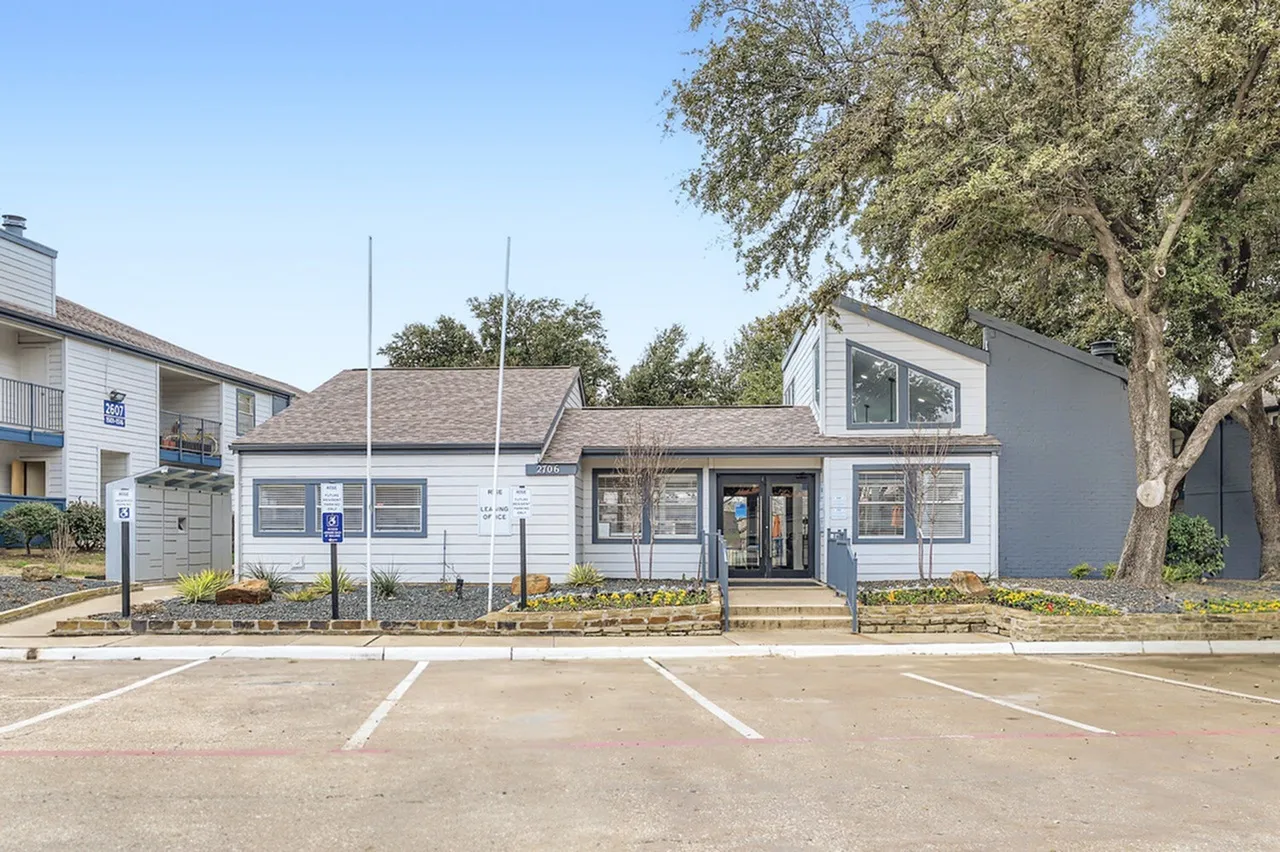 Leasing office exterior, white facade, glass entry doors, landscaping, large tree, parking spaces