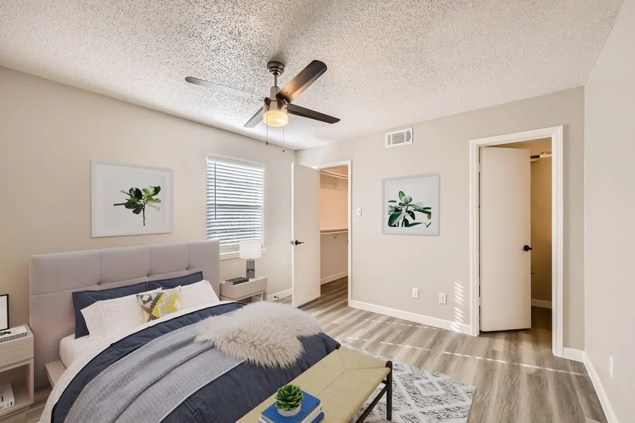 Primary bedroom, upholstered headboard, ceiling fan with light, wood-style plank flooring, plantation shutters