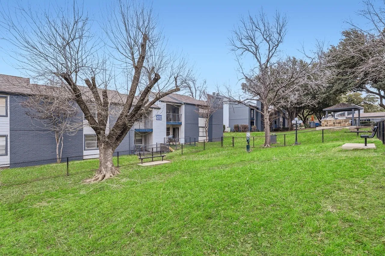 Community courtyard with green lawn, bare trees, residential buildings, clear sky