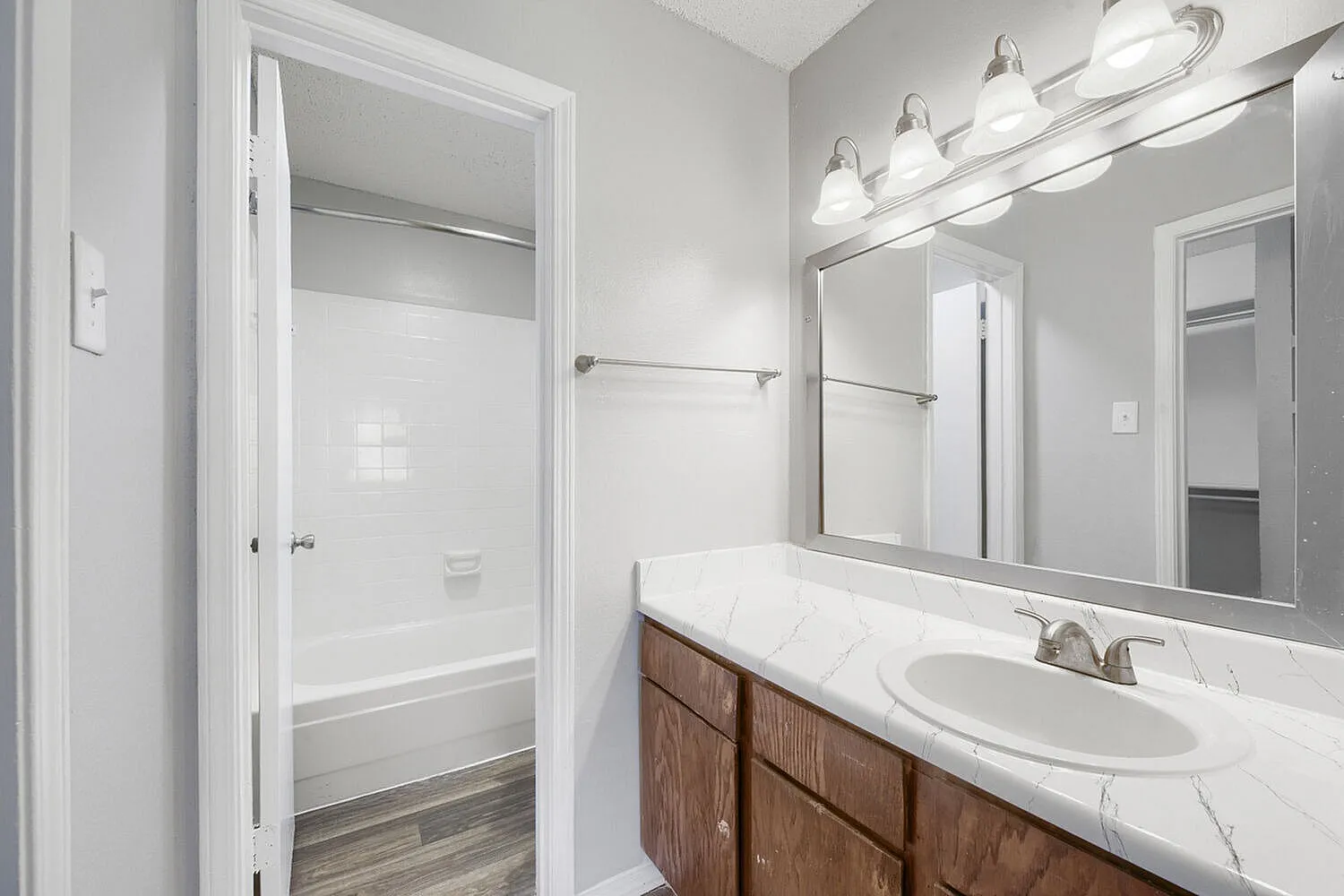 Primary bathroom, wood-style vanity cabinetry, white marble countertop, oval sink, chrome fixtures, framed mirror, wall sconces