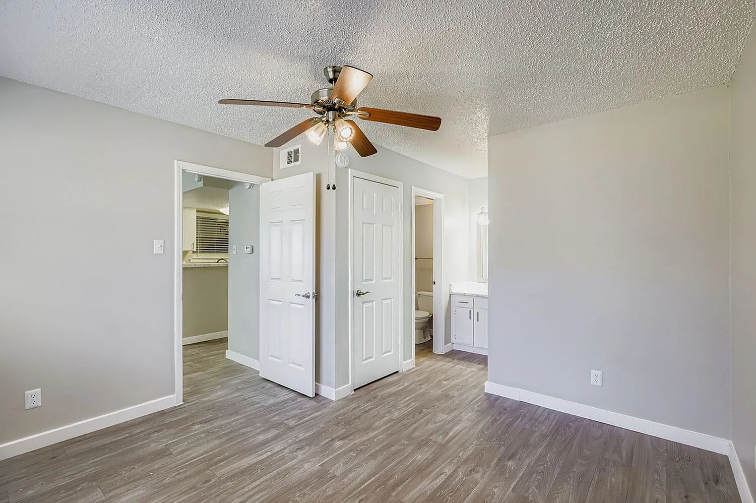 Primary bedroom, wood-style plank flooring, ceiling fan, double closet doors, ensuite bathroom