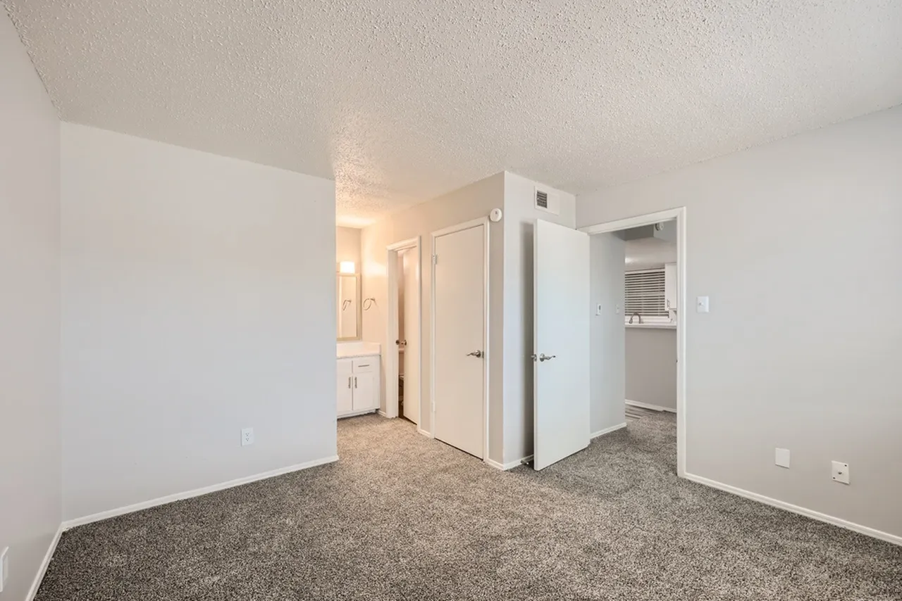 Bedroom, gray carpet flooring, white walls, closet doors, laundry area visible