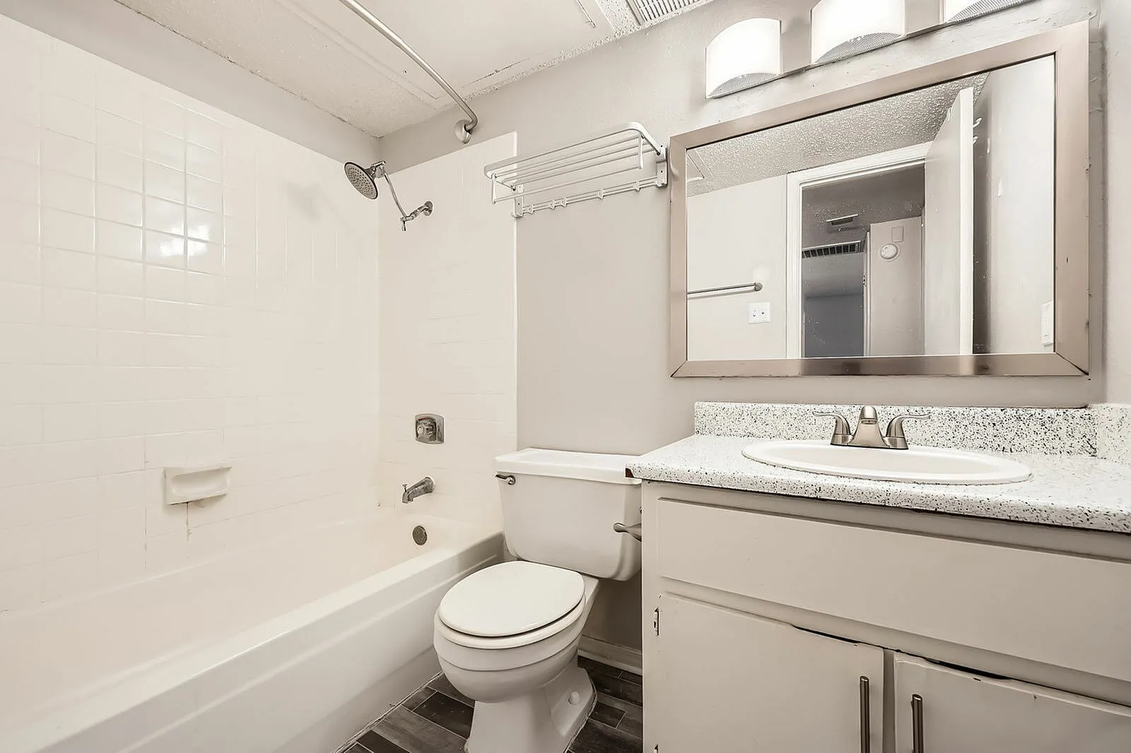 Bathroom, white tile surround, vanity with speckled countertops, framed mirror, wood-style plank flooring