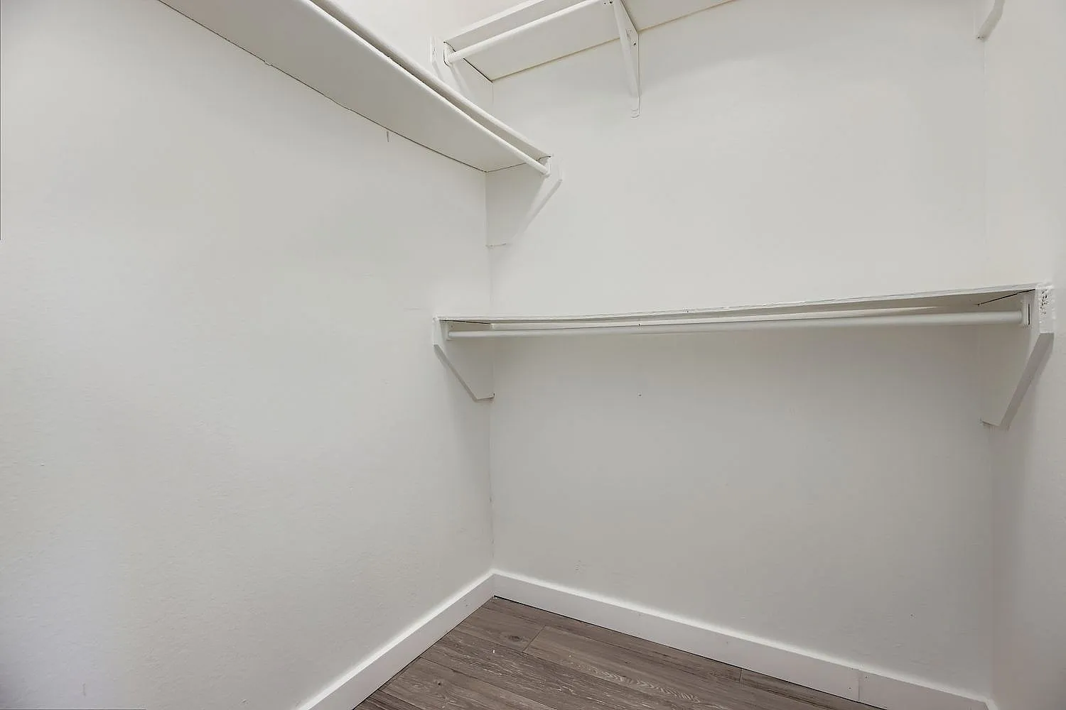 Walk-in closet, metal hanging rods, white walls, wood-style plank flooring