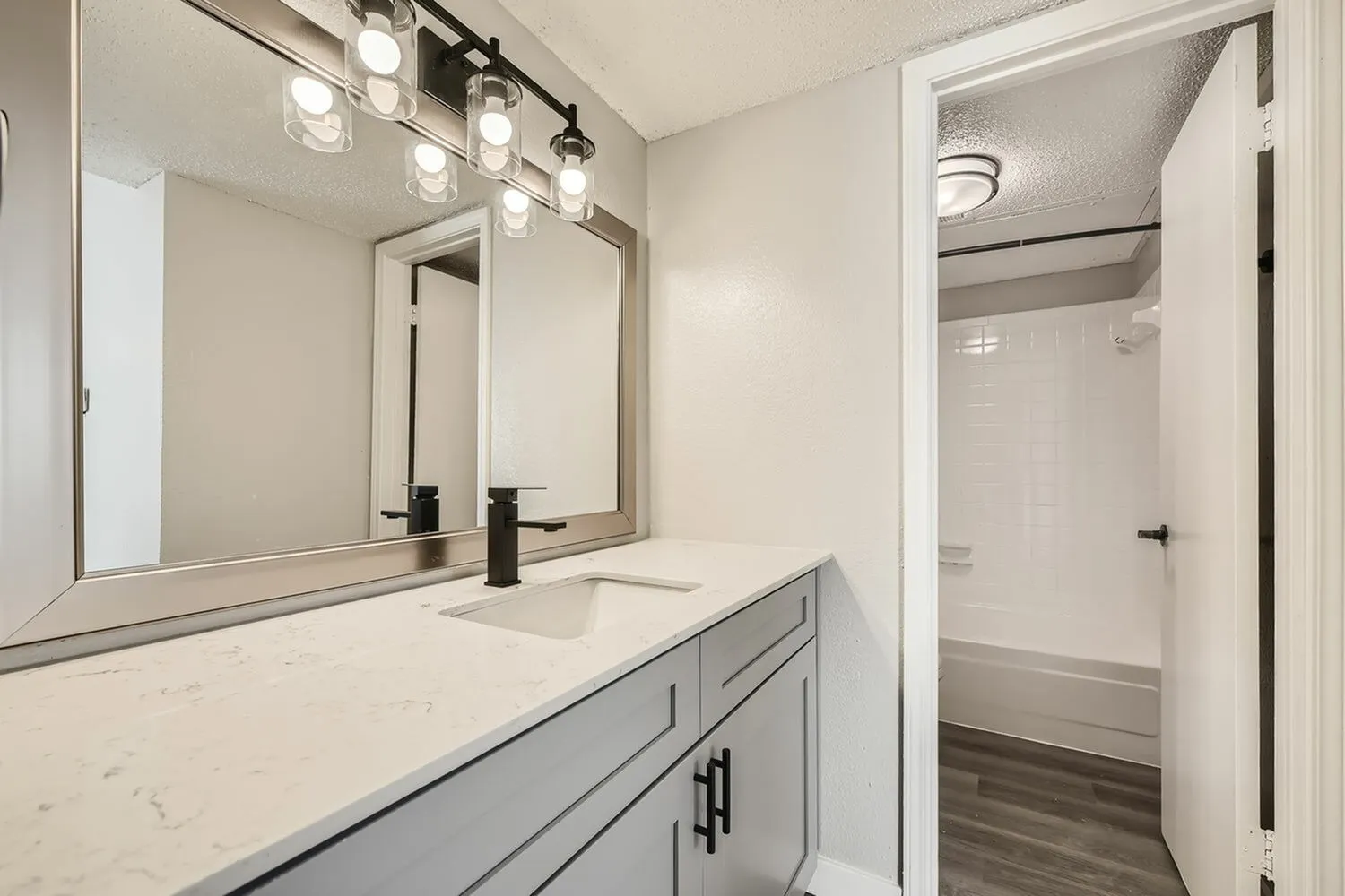 Primary bathroom, gray vanity cabinetry, quartz countertop, framed mirror, vanity lighting