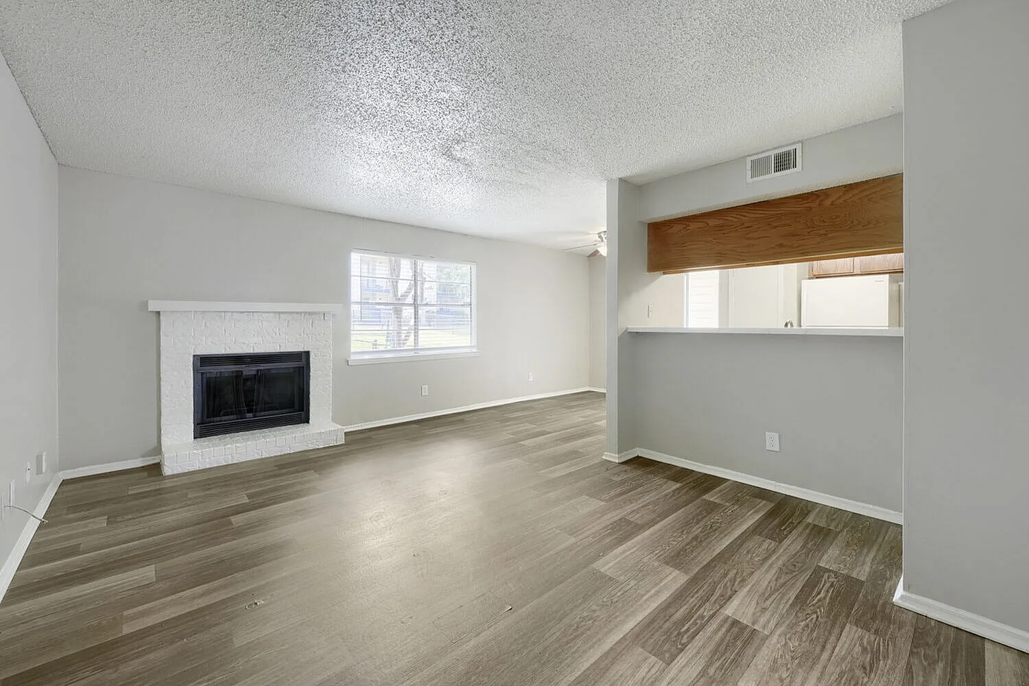 Living room, wood-style plank flooring, fireplace with dark surround, large window, textured ceiling