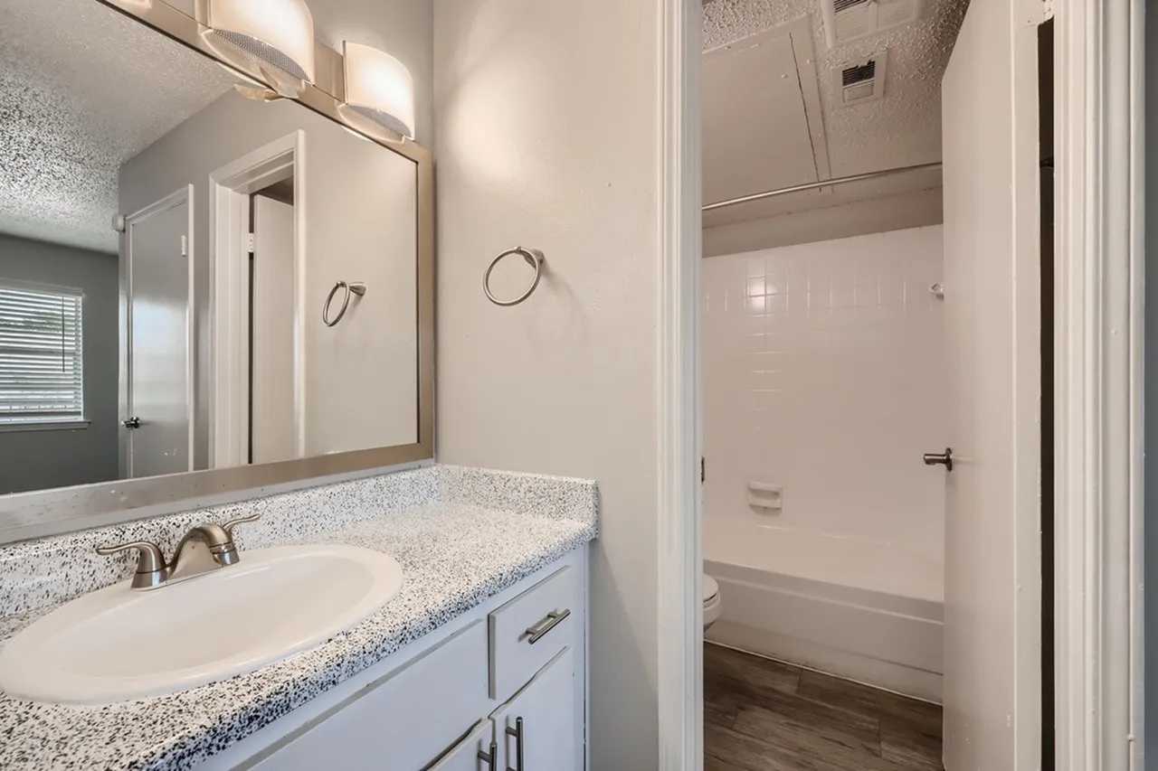 Bathroom, quartz countertops, speckled vanity, large mirror with lighting, tile shower
