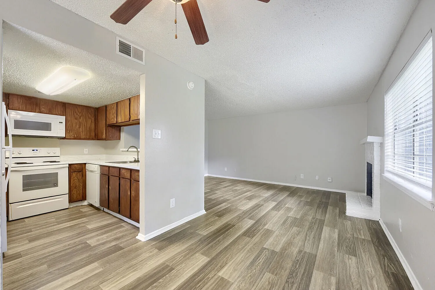 Kitchen and living room, wood cabinetry, white appliances, wood-style plank flooring, ceiling fan