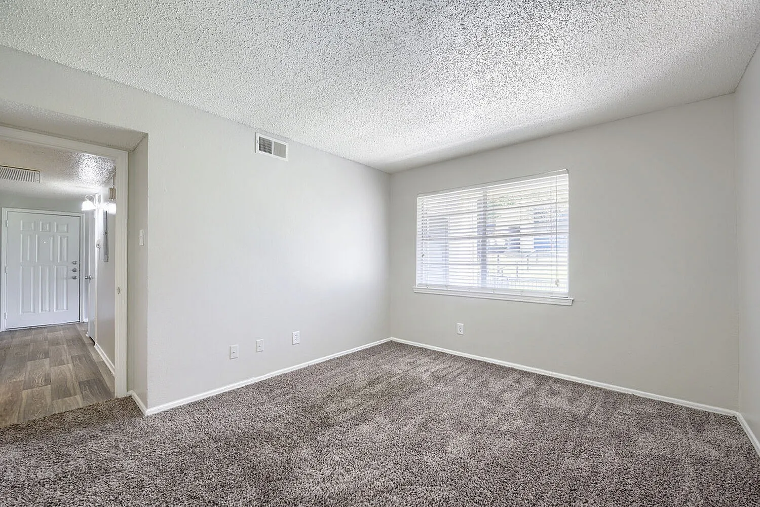 Bedroom, gray carpet flooring, textured ceiling, bright window with blinds, white walls