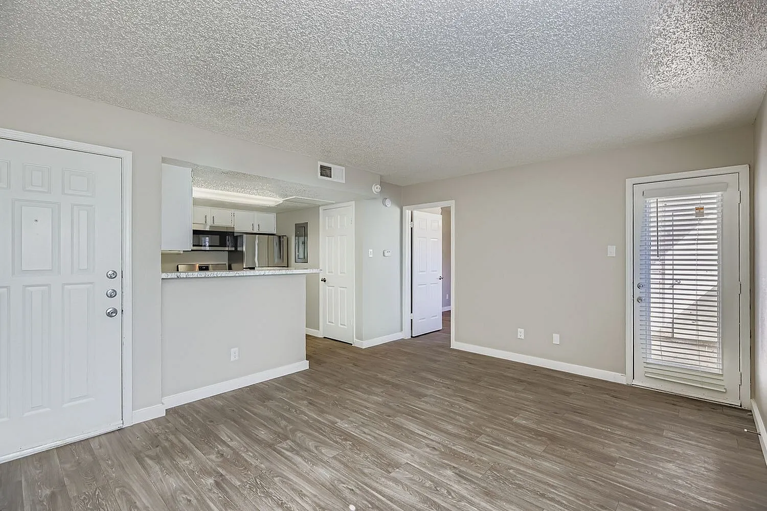 Open living space, wood-style plank flooring, white kitchen cabinetry, glass door to patio