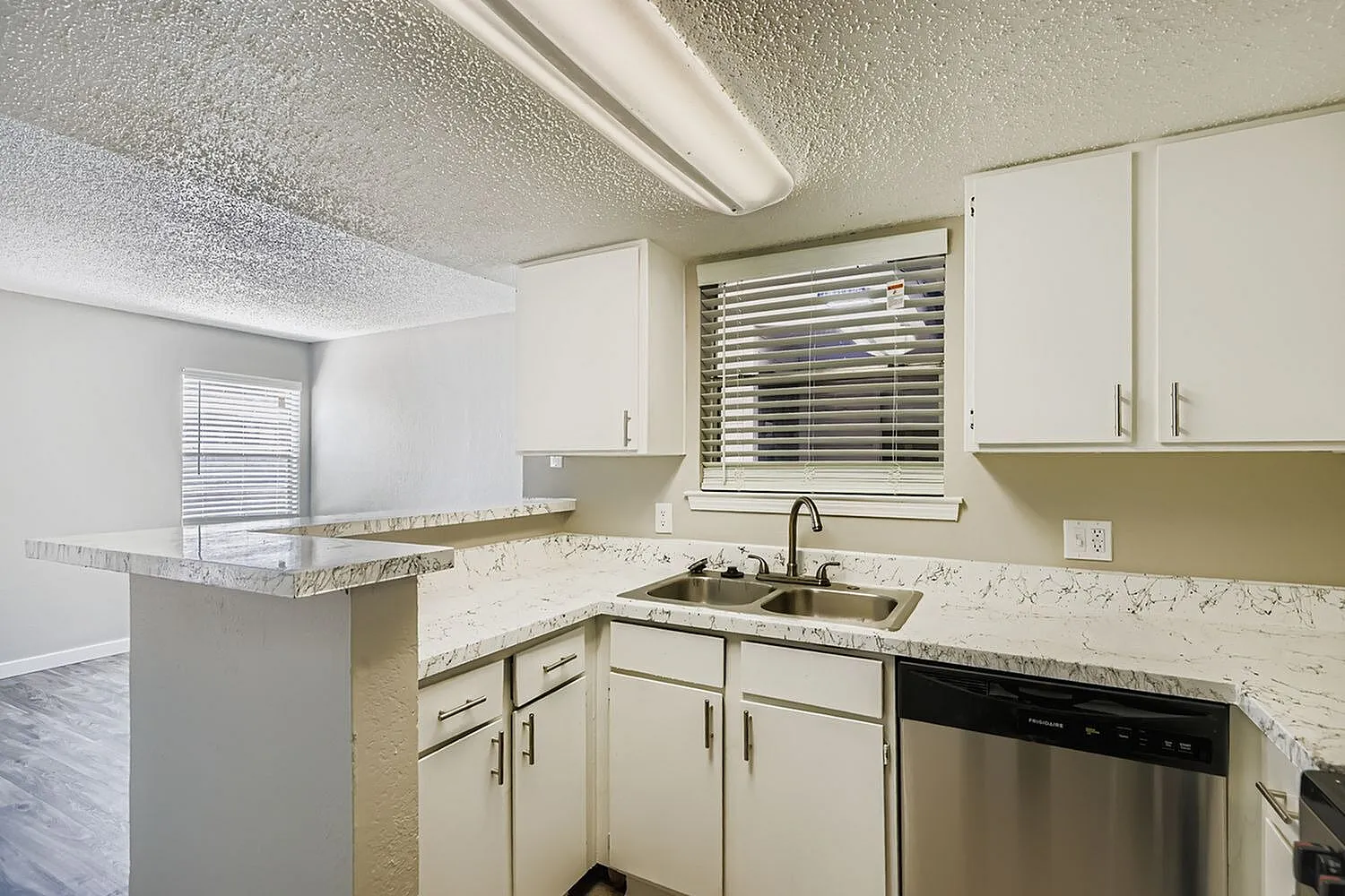 Kitchen, cream shaker cabinetry, speckled quartz countertops, stainless steel sink and dishwasher, window with blinds