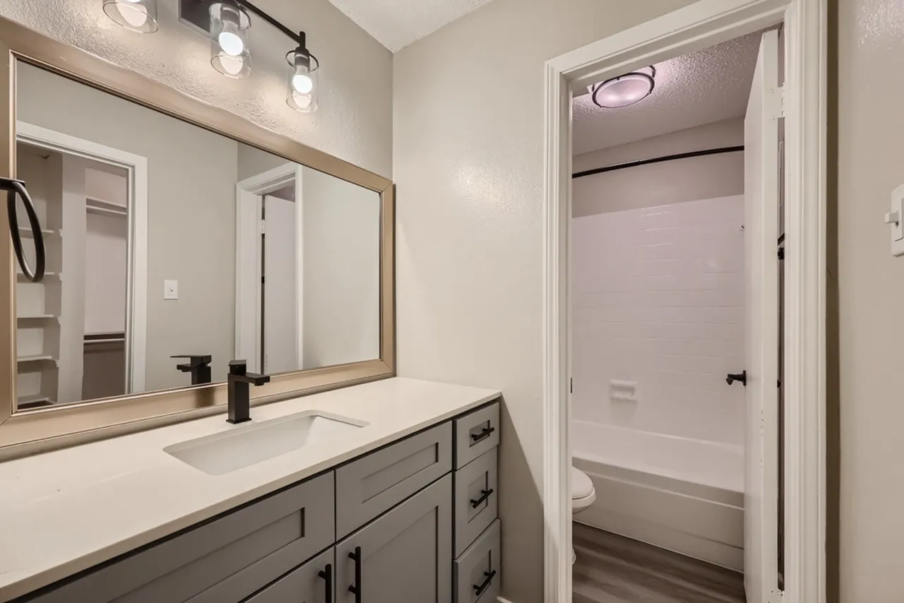 Primary bathroom, double vanity with gray cabinetry, white countertops, framed mirror, chrome fixtures
