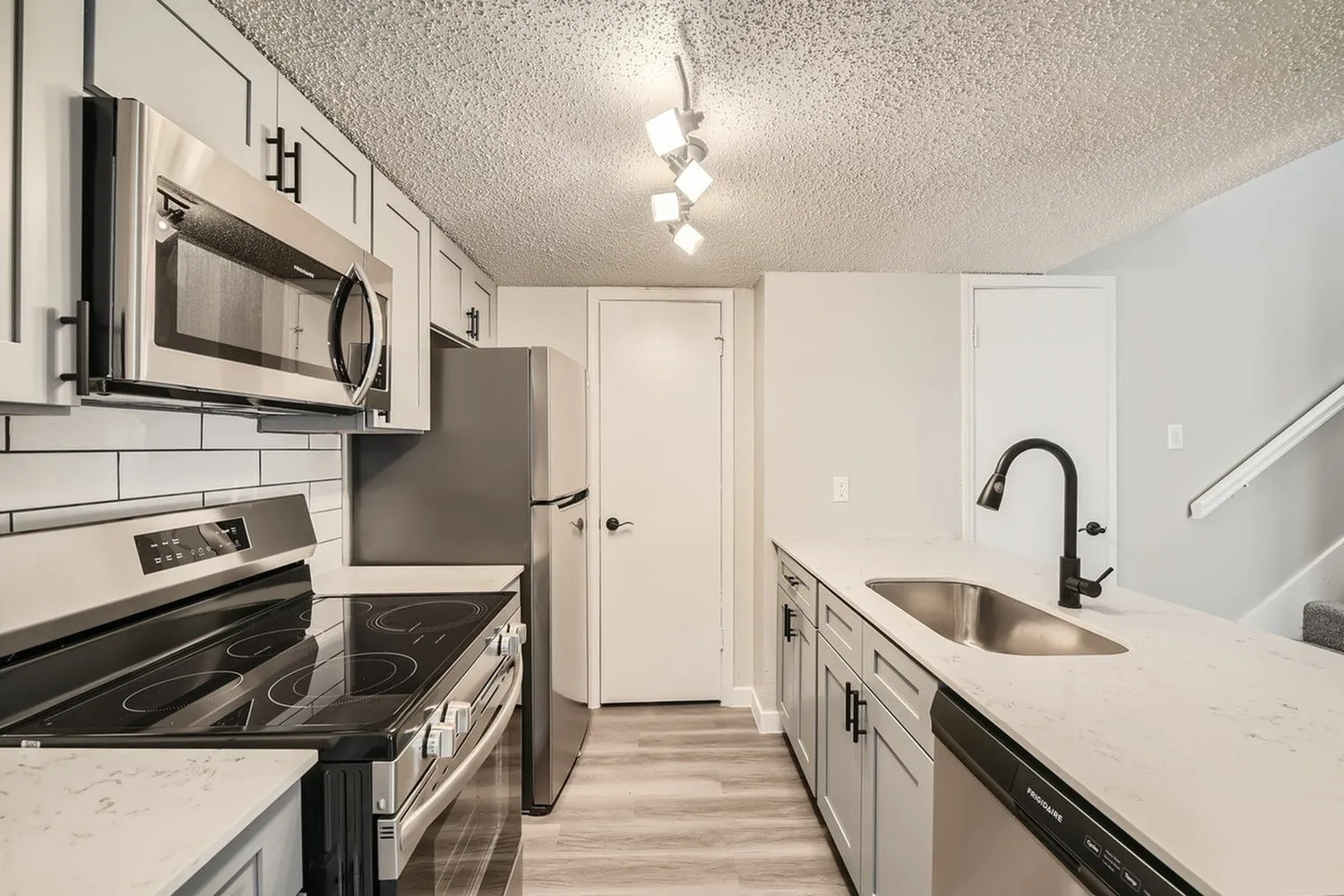 Kitchen, white shaker cabinetry, quartz countertops, stainless appliances, wood-style plank flooring