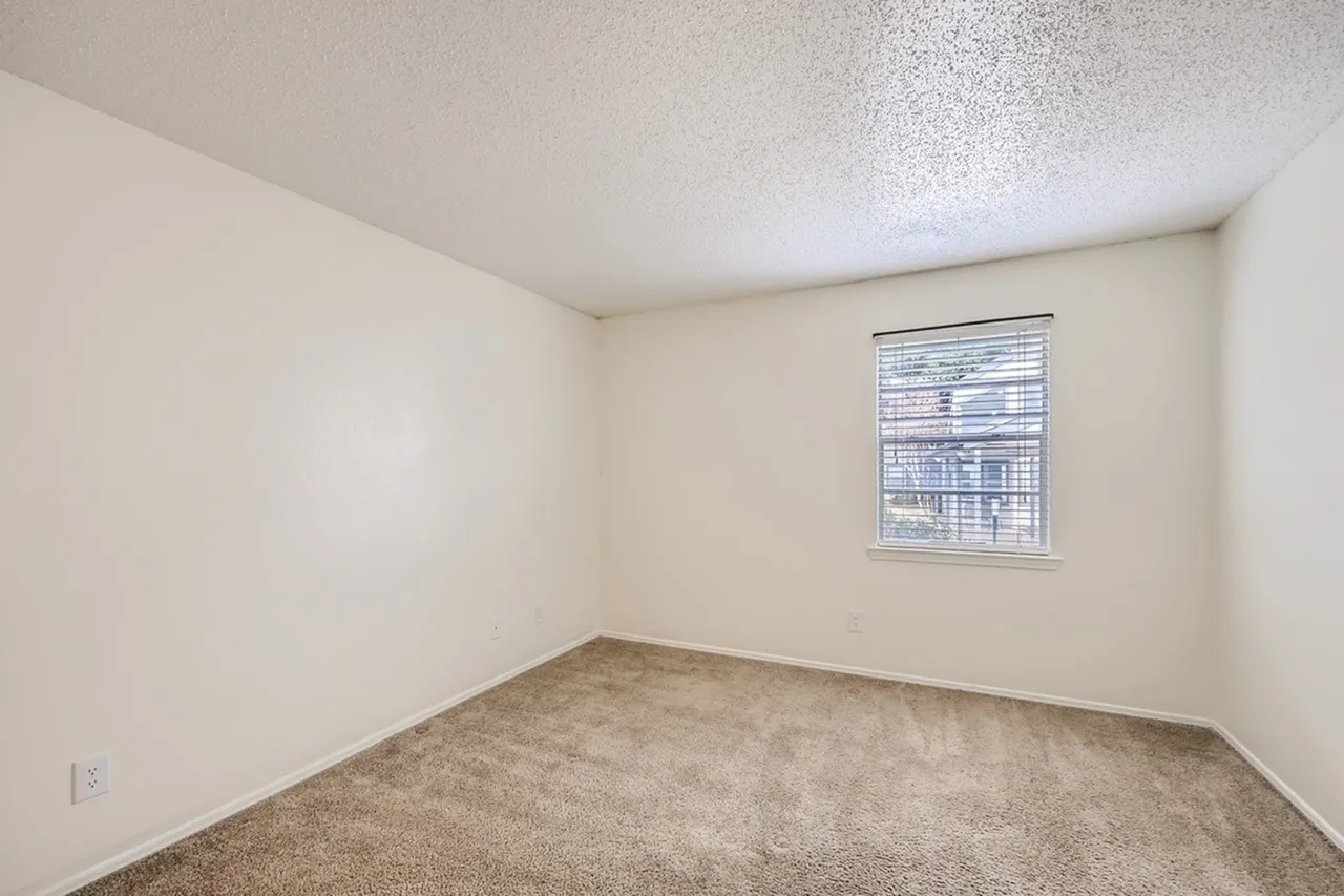 Bedroom, beige walls, textured ceiling, carpet flooring, window with blinds
