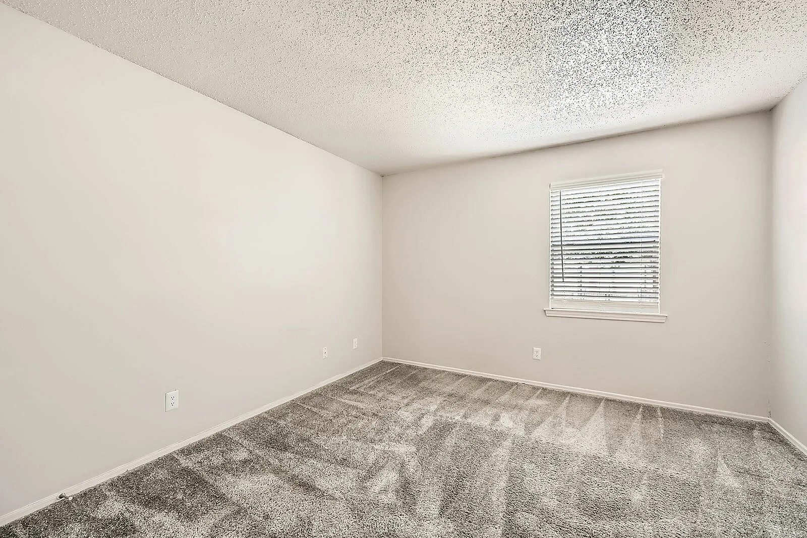 Empty bedroom, gray carpet flooring, textured ceiling, window with blinds