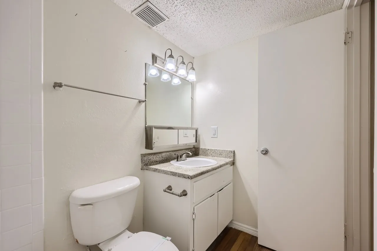 Bathroom, white vanity cabinet, gray speckled countertop, mirror with lighting fixture