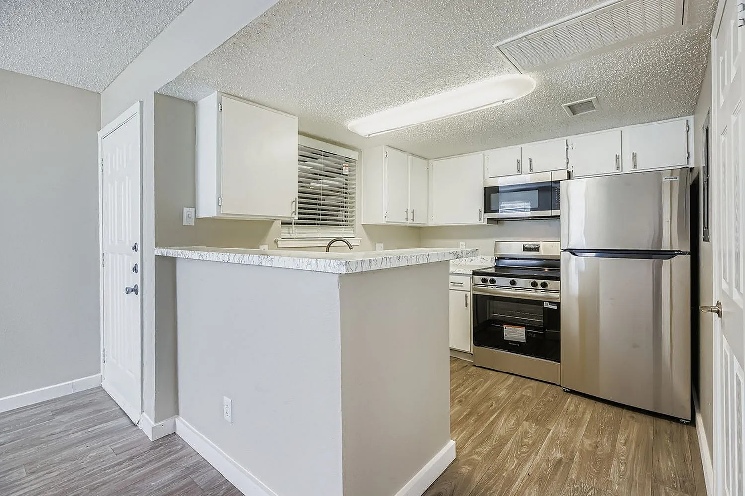 Kitchen, white cabinetry, gray quartz countertops, stainless steel appliances, wood-style plank flooring