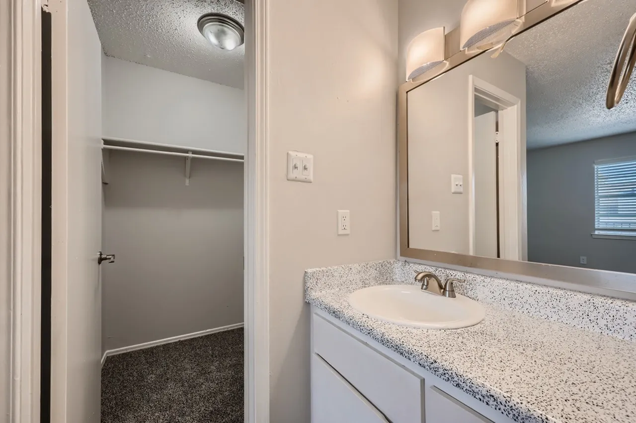 Bathroom, speckled quartz countertops, white vanity, framed mirror, shower stall