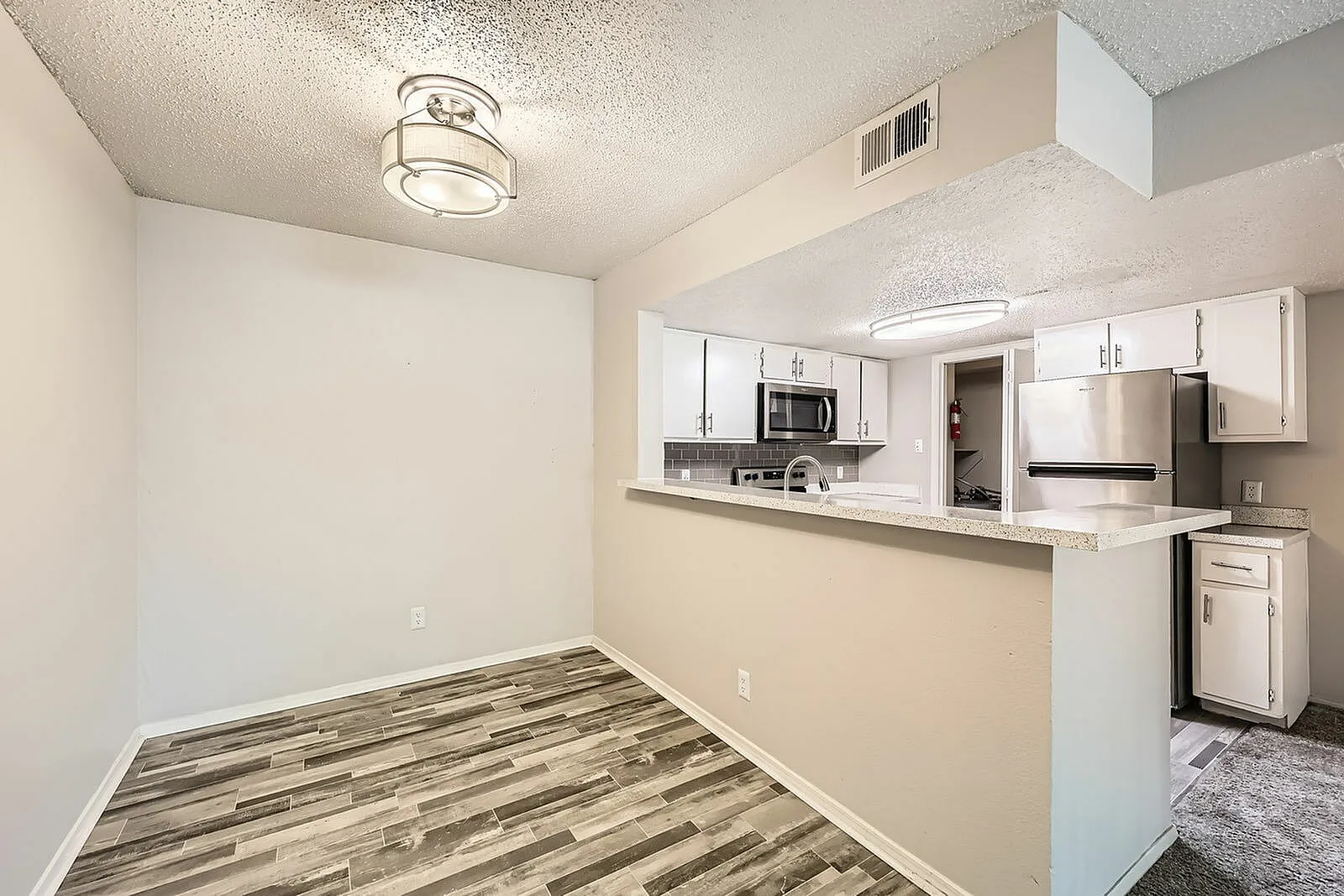 Dining room with wood-style plank flooring, white cabinetry, stainless appliances, kitchen pass-through