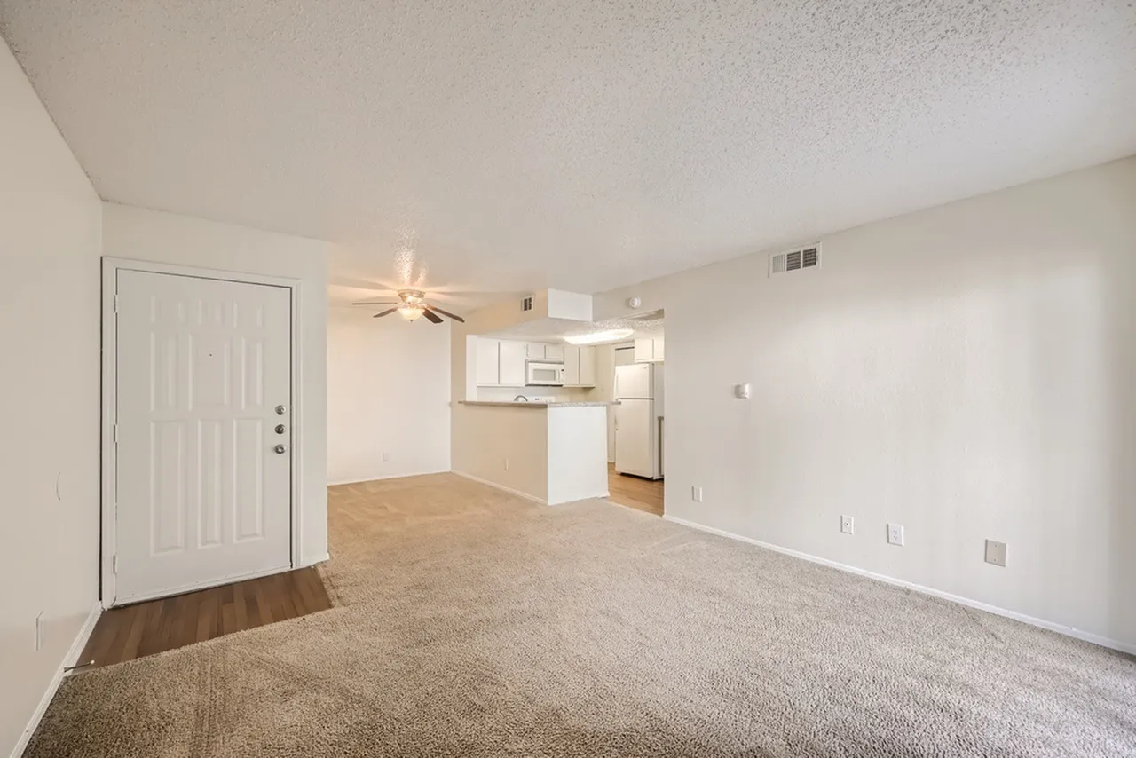 Living room with wood-style plank flooring, ceiling fan, open kitchen with white cabinetry, stainless appliances, entry door