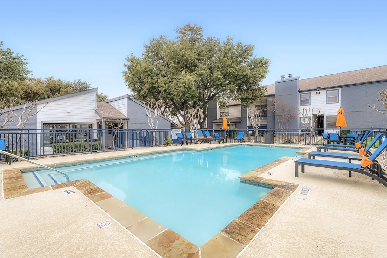 Outdoor swimming pool, lounge seating, landscaping, blue fencing, residential buildings