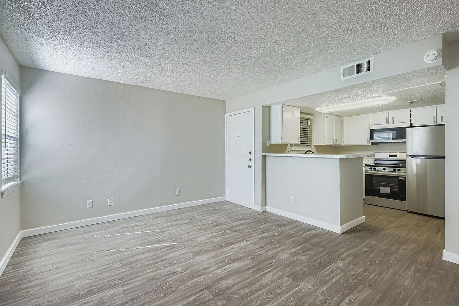Living room and kitchen, wood-style plank flooring, white cabinetry, stainless appliances, granite countertops