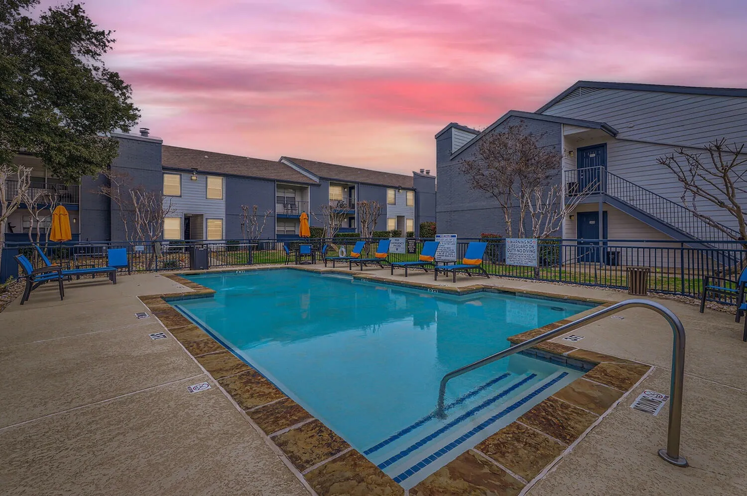 Outdoor swimming pool, lounge seating, modern apartment buildings, twilight sky