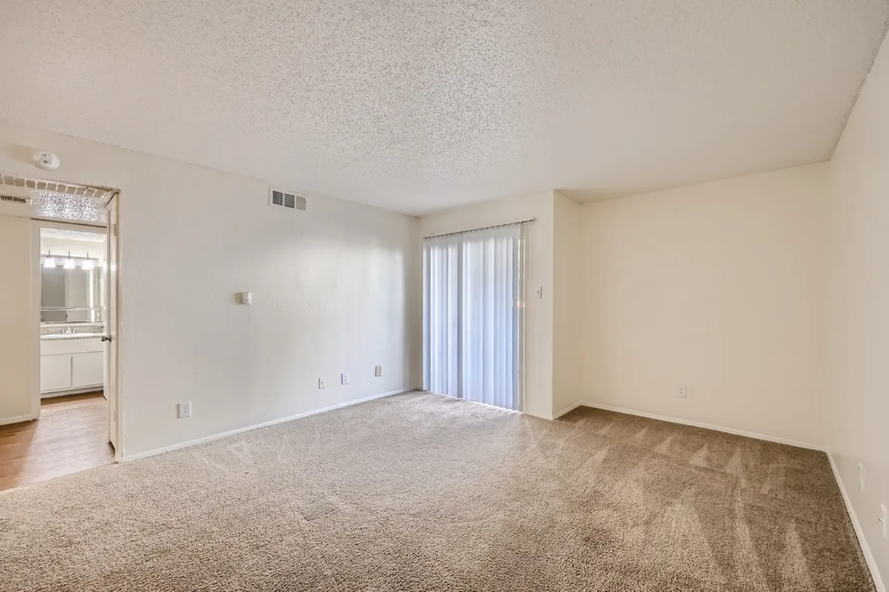 Living room with wood-style plank flooring, vertical blinds, entry to kitchen area