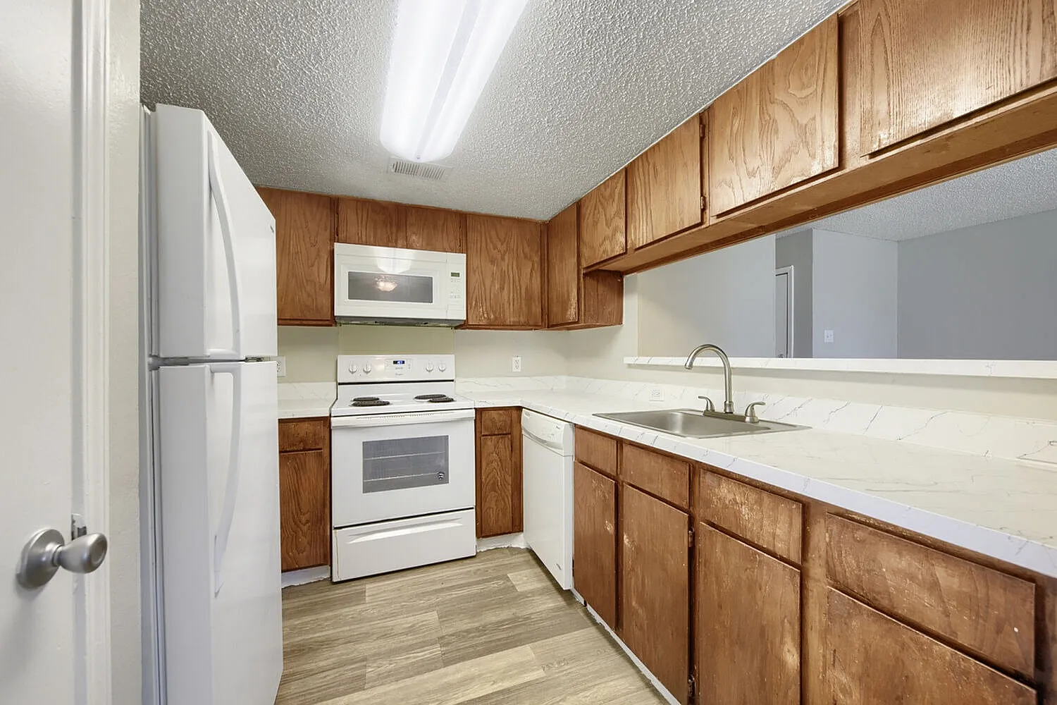 Kitchen, wood cabinetry, white countertops, white appliances, wood-style plank flooring