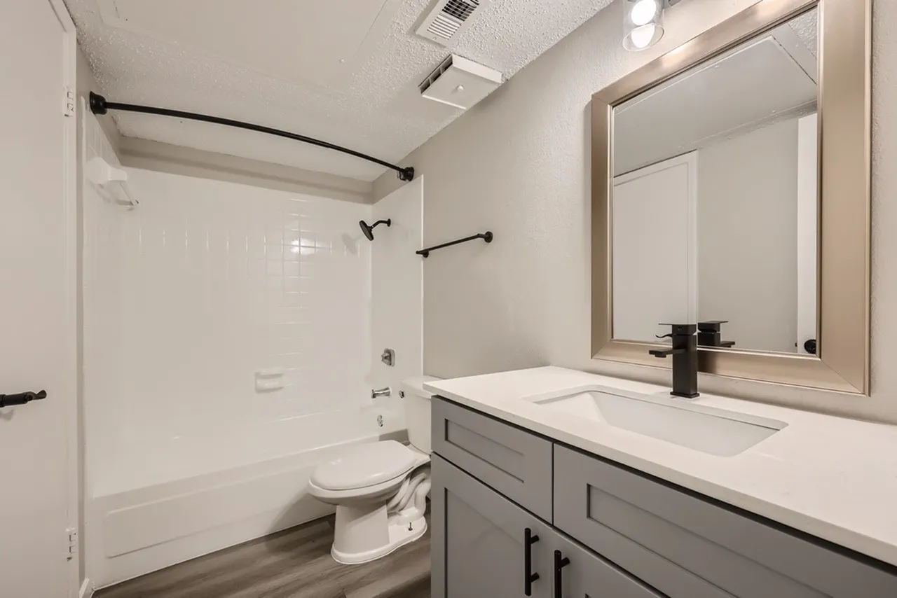 Bathroom, gray cabinetry, white quartz countertop, framed mirror, white subway tile shower