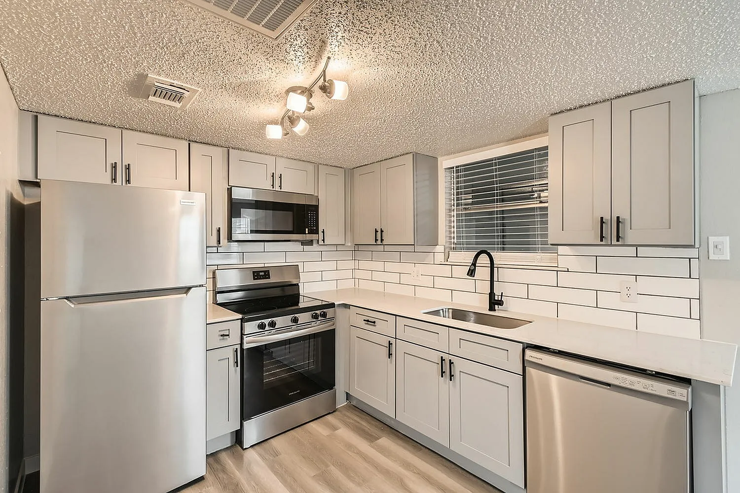 Kitchen, white shaker cabinetry, white subway tile backsplash, stainless appliances, wood-style plank flooring