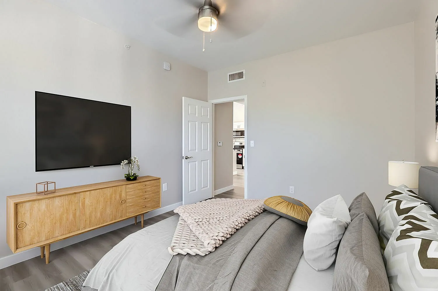 Primary bedroom, wood-style media console, wall-mounted TV, gray bedding, wood-style plank flooring