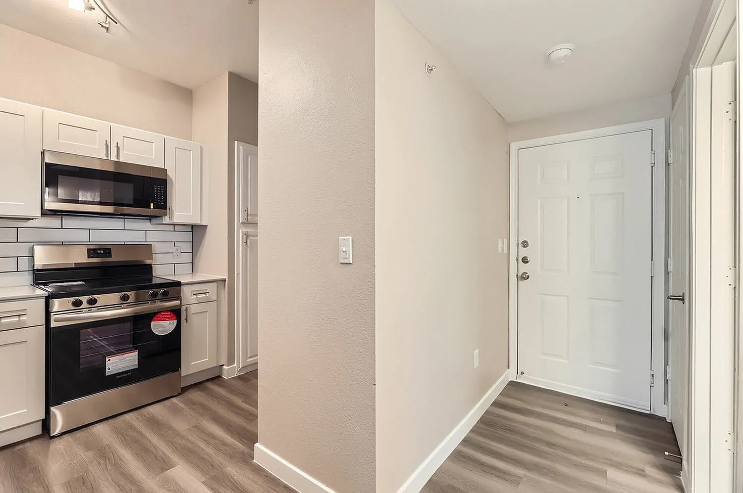 Kitchen with white shaker cabinetry, stainless appliances, subway tile backsplash, wood-style plank flooring, white entry door