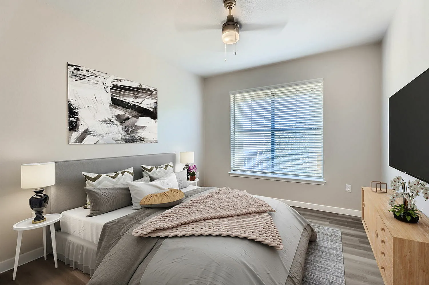 Primary bedroom, gray upholstered headboard, wood-style plank flooring, pendant ceiling fixture, large window with blinds