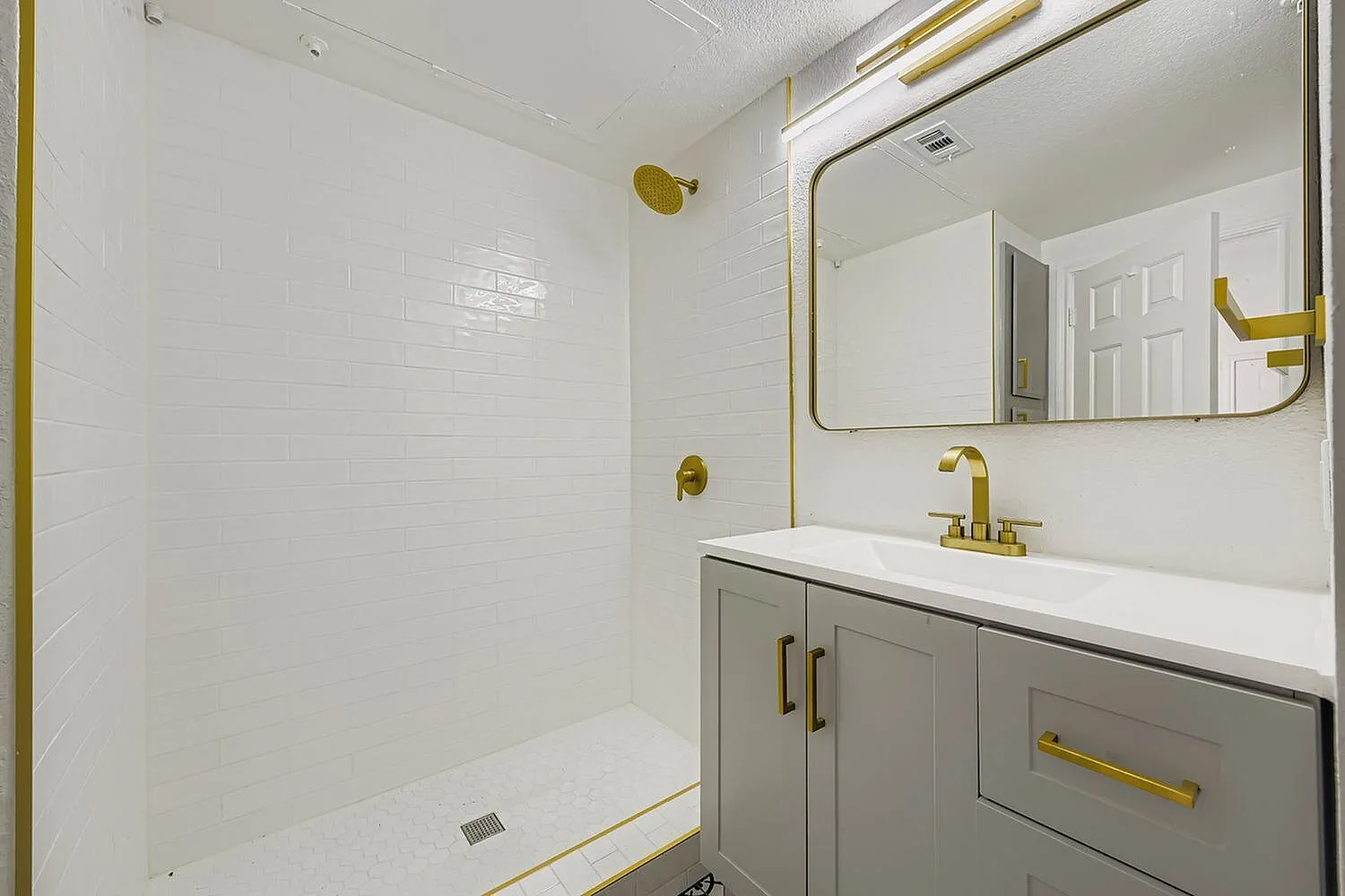 Bathroom, gray cabinetry, white quartz countertops, gold fixtures, mirror, subway tile walls