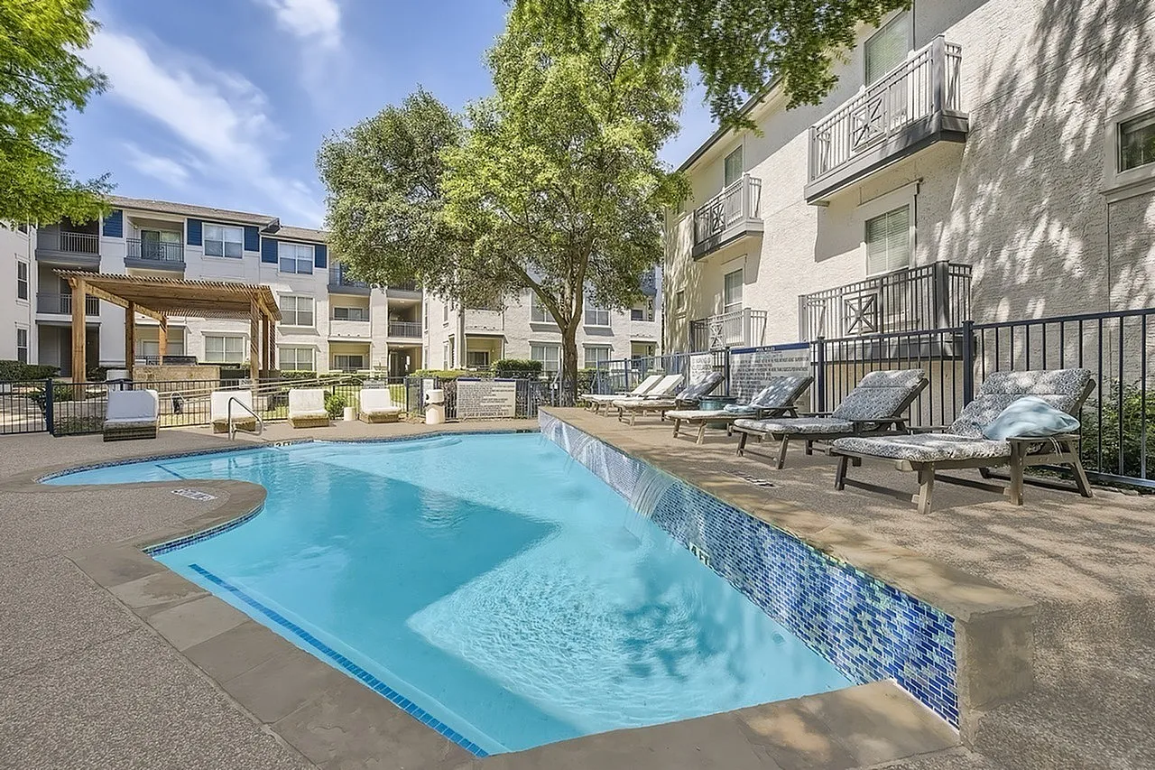 Swimming pool, lounge chairs, shade trees, residential buildings, black metal railings