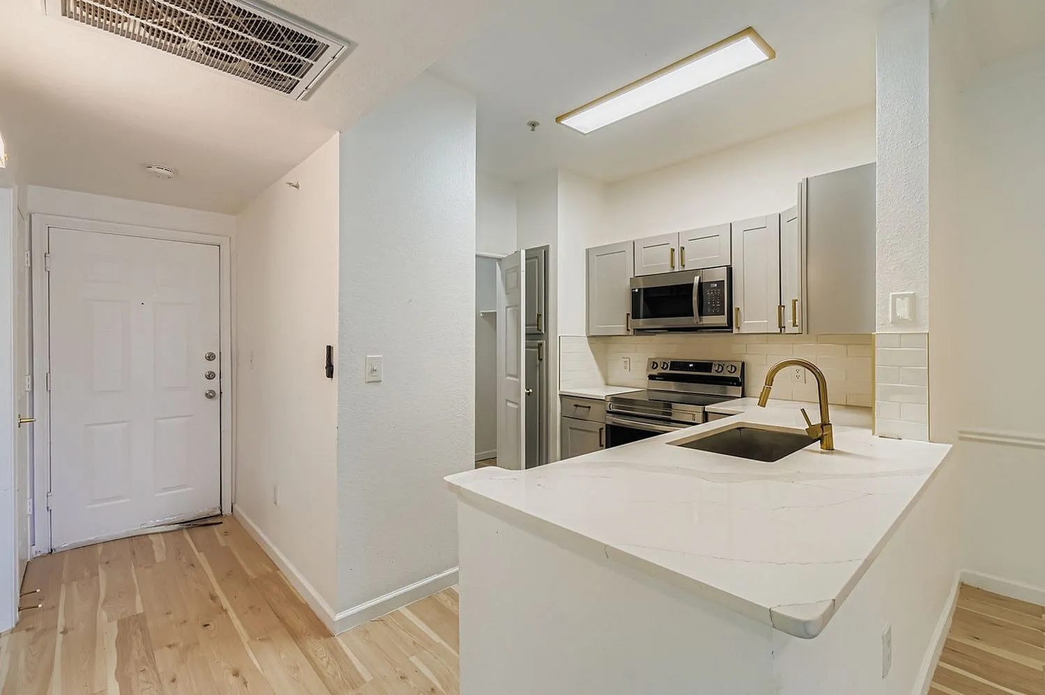 Kitchen with white shaker cabinetry, quartz countertops, stainless appliances, wood-style plank flooring, entry door