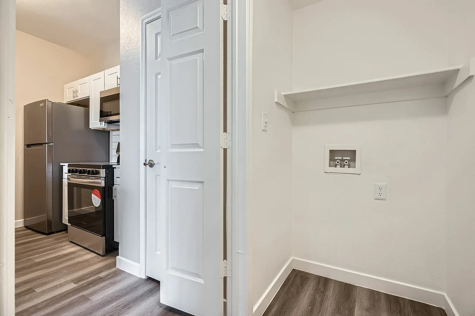 Kitchen with stainless appliances, wood-style plank flooring, white six-panel door, floating shelf